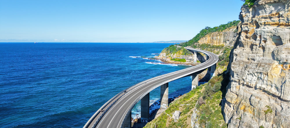 Sea Cliff Bridge curving over the ocean beside sandstone cliffs, Clifton, New South Wales - fine art photography print by Adam Gormley