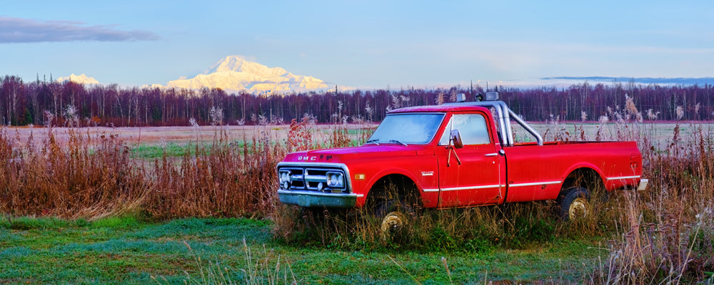 Old red pickup truck in long grass with Denali on the horizon, Alaska - fine art photography print by Adam Gormley