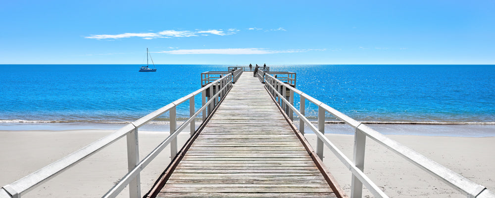 Torquay Jetty over clear blue water with a yacht, Hervey Bay, Queensland - fine art photography print by Adam Gormley