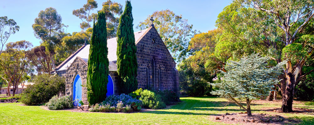 Bluestone church with blue doors among cypress and gum trees at Bulla, Victoria - fine art photography print by Adam Gormley
