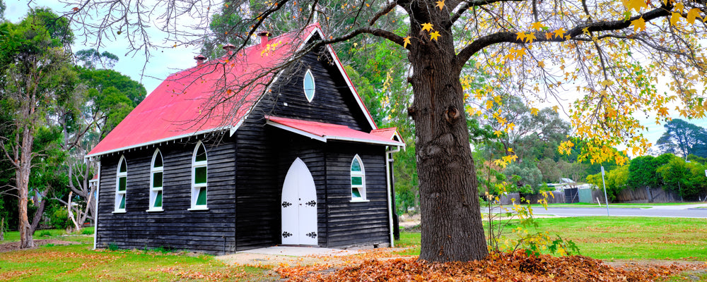 Black timber church with a red roof under autumn leaves at Cann River, Victoria - fine art photography print by Adam Gormley