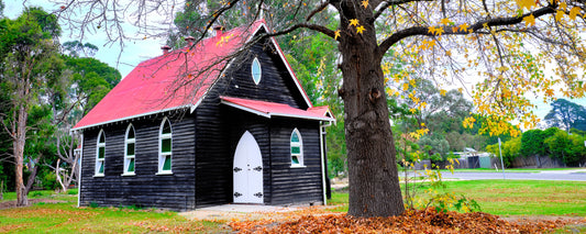 Black timber church with a red roof under autumn leaves at Cann River, Victoria - fine art photography print by Adam Gormley
