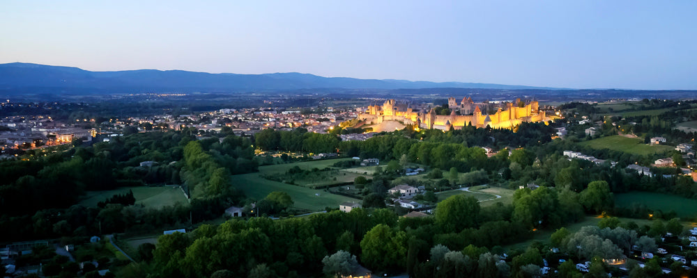 The lit walls of Carcassonne glowing above the countryside at dusk, France - fine art photography print by Adam Gormley