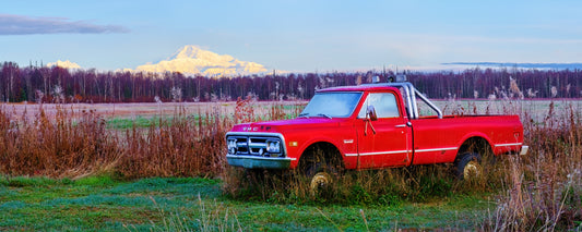 Old red pickup truck in long grass with Denali on the horizon, Alaska - fine art photography print by Adam Gormley