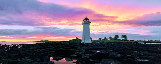 Port Fairy lighthouse on black rocks under a pink and purple sunset sky, Victoria - fine art photography print by Adam Gormley