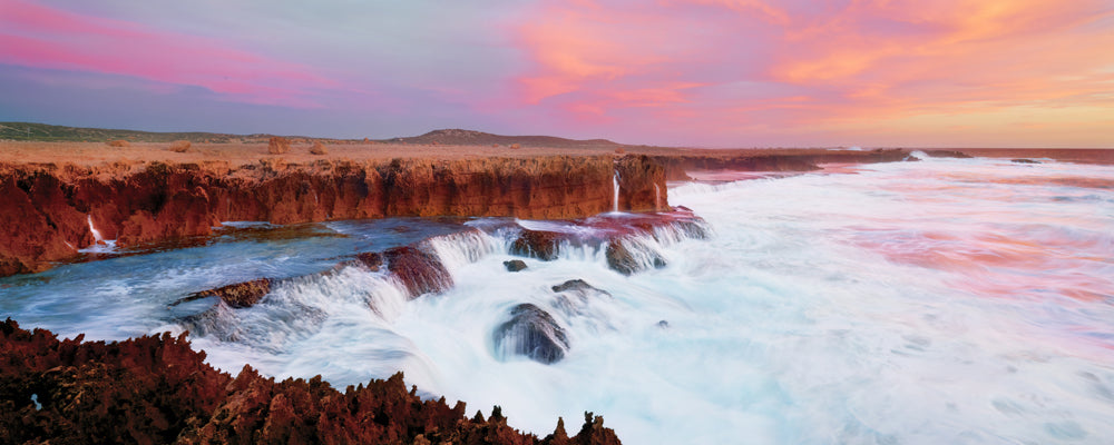 Waves over red rock ledges under a pink sunset sky on the Quobba coast, Western Australia - fine art photography print by Adam Gormley