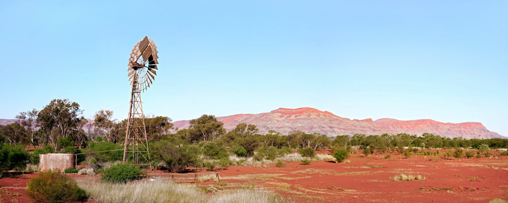 Old windmill on red dirt with the Hamersley Range behind, Pilbara, Western Australia - fine art photography print by Adam Gormley